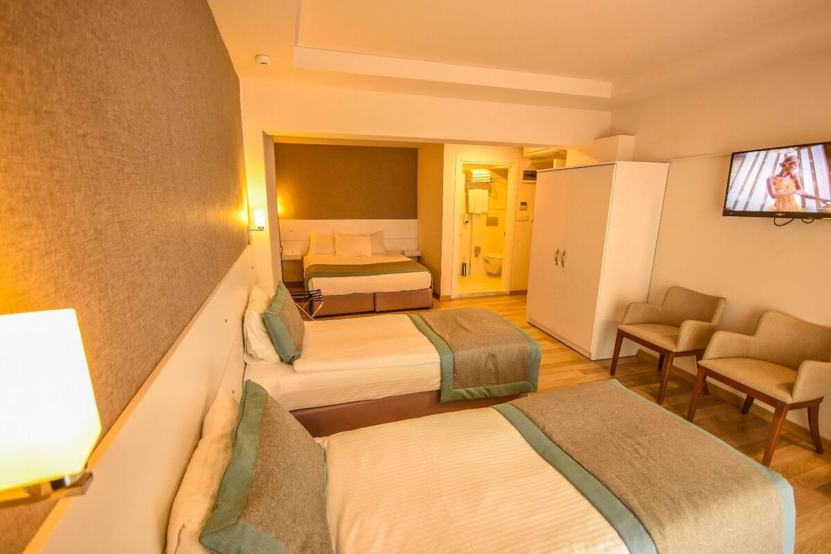 A hotel room with two beds, a TV, a wardrobe, and a seating area.
