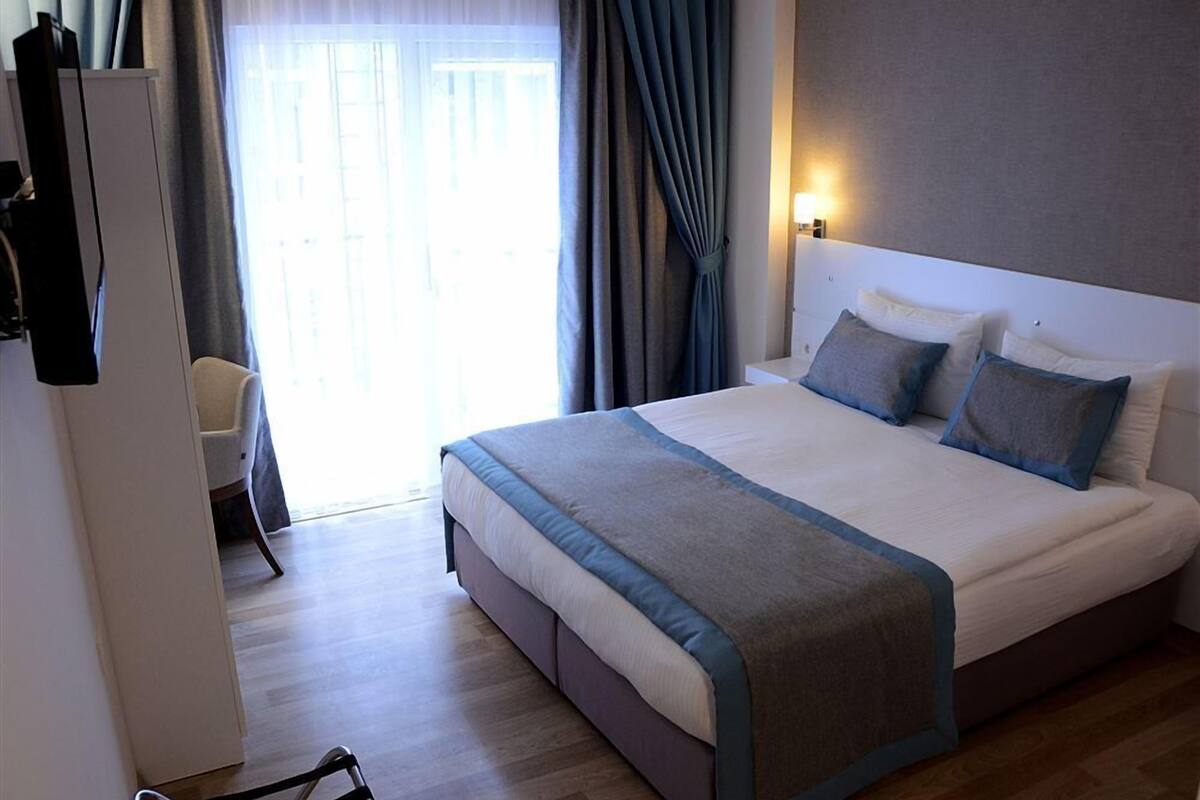 A hotel room with a large bed, a bedside table, a chair, and a window with curtains.