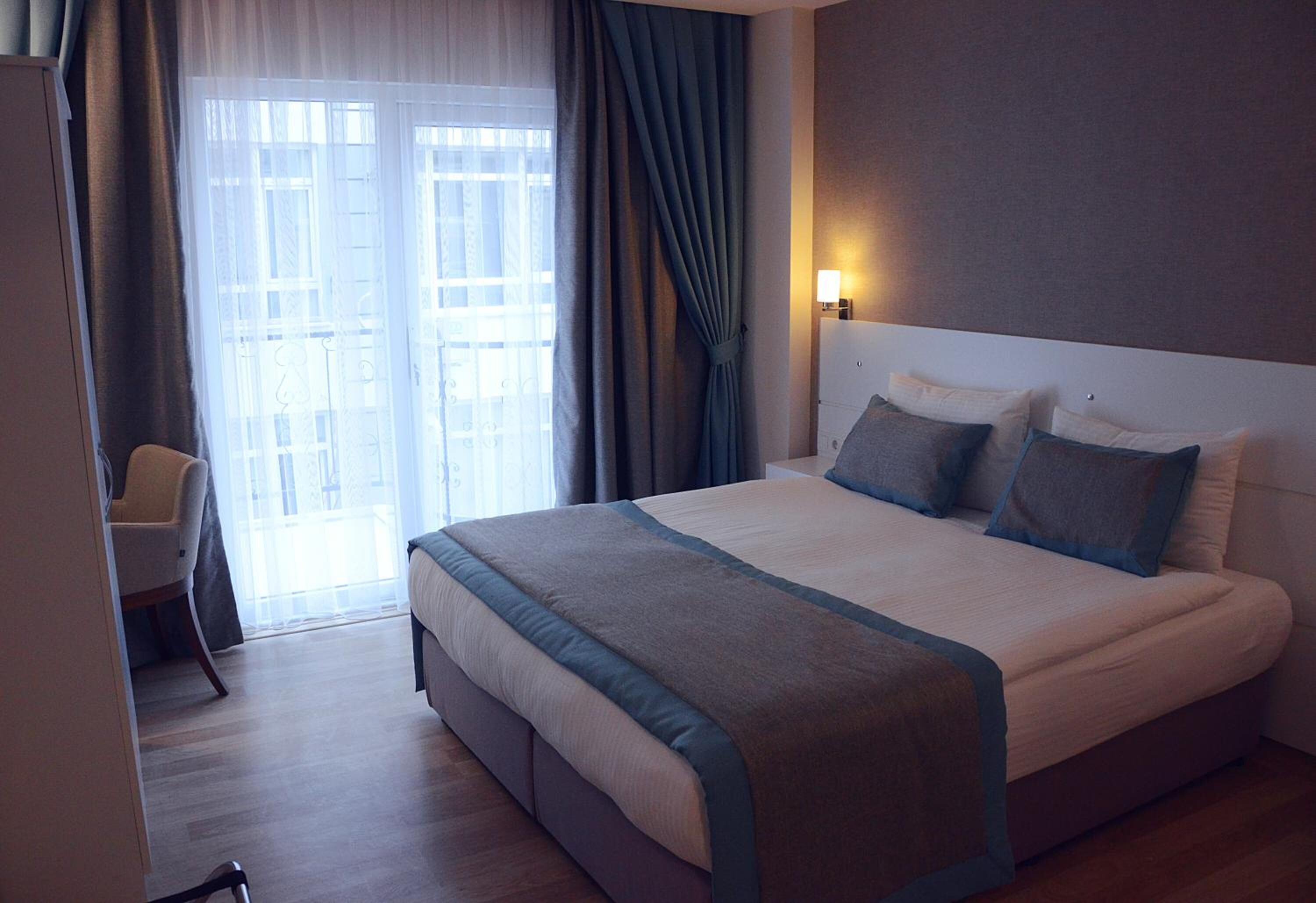 A hotel room with a large bed, a chair, a desk, and a window with curtains.