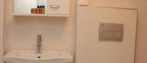 A bathroom with a white sink, mirror, and toilet. There is a trash can next to the toilet.