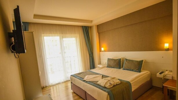 A hotel room with a large bed, a television, a desk with a phone, and a window with curtains. - Parion House Hotel (Çanakkale)