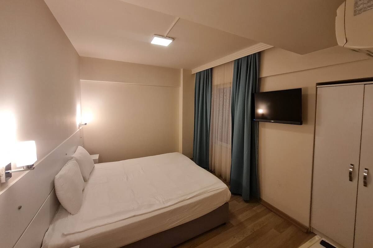 A hotel room with a bed, a flat-screen TV mounted on the wall, a wardrobe, and a ceiling light.