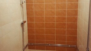 A small, enclosed shower area with beige and brown tiles, a metal showerhead, and a handheld shower attachment. - Patrician Hotel (Trangsund)