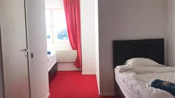 Habitación de hotel con alfombra roja, cama con ropa de cama blanca, cabecera negra y ventana con cortina roja.