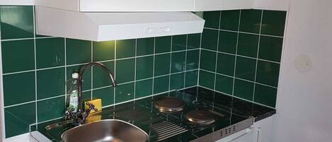 A compact kitchen with a sink, stove, and white cabinets.