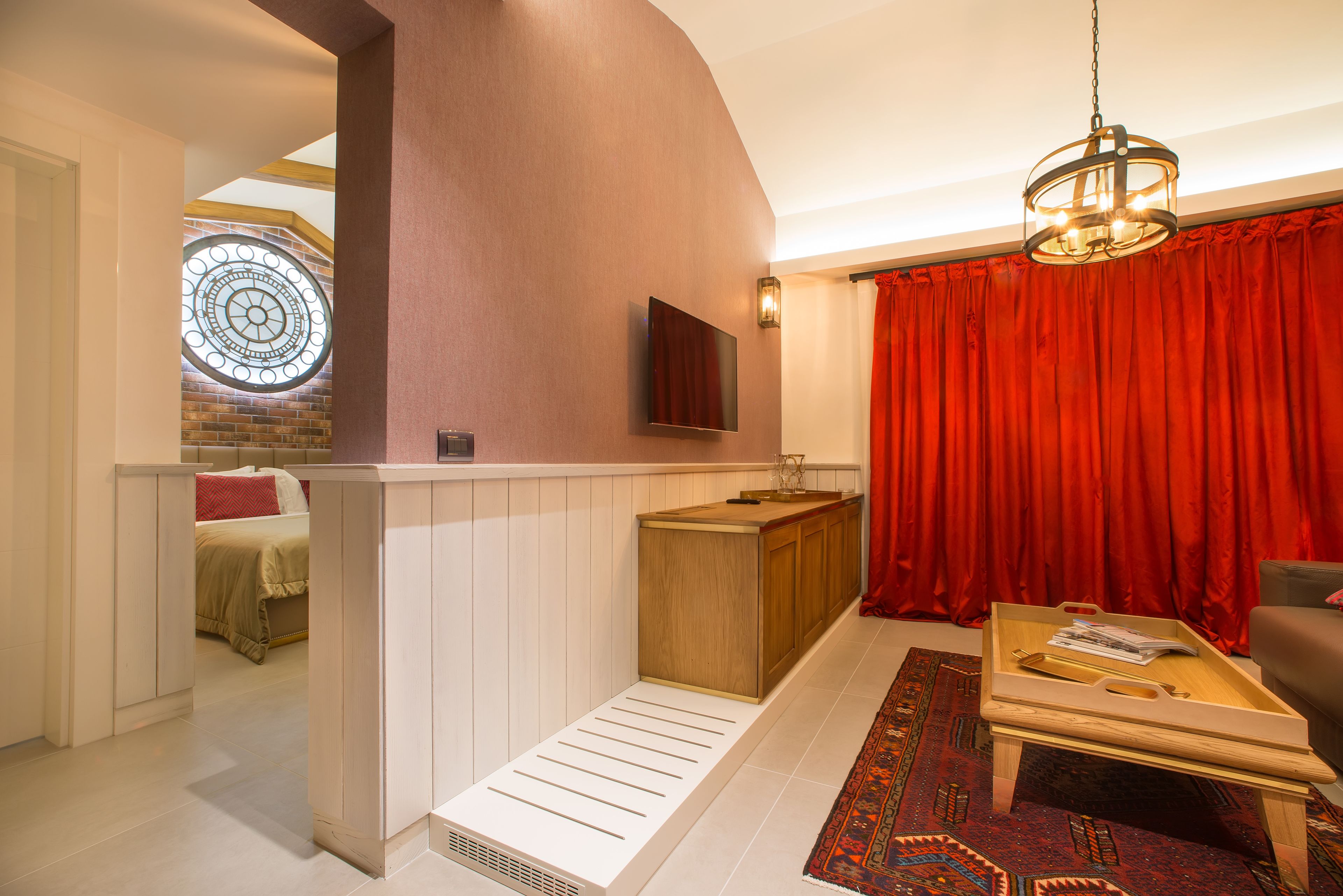 A modern living room with a wooden bench, a red curtain, a patterned rug, and a television mounted on the wall.