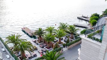 A rooftop terrace with outdoor seating, palm trees, and a view of the sea.