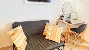 A modern living room with a grey sofa, striped pillows, a small wooden table, a black chair, a round mirror, and a framed menu on the wall. - Bel Momento (Zakynthos)