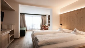 A modern hotel room with two beds, a wooden headboard, a desk, and a view of the city through large windows. - Family Resort Rainer (Sesto)