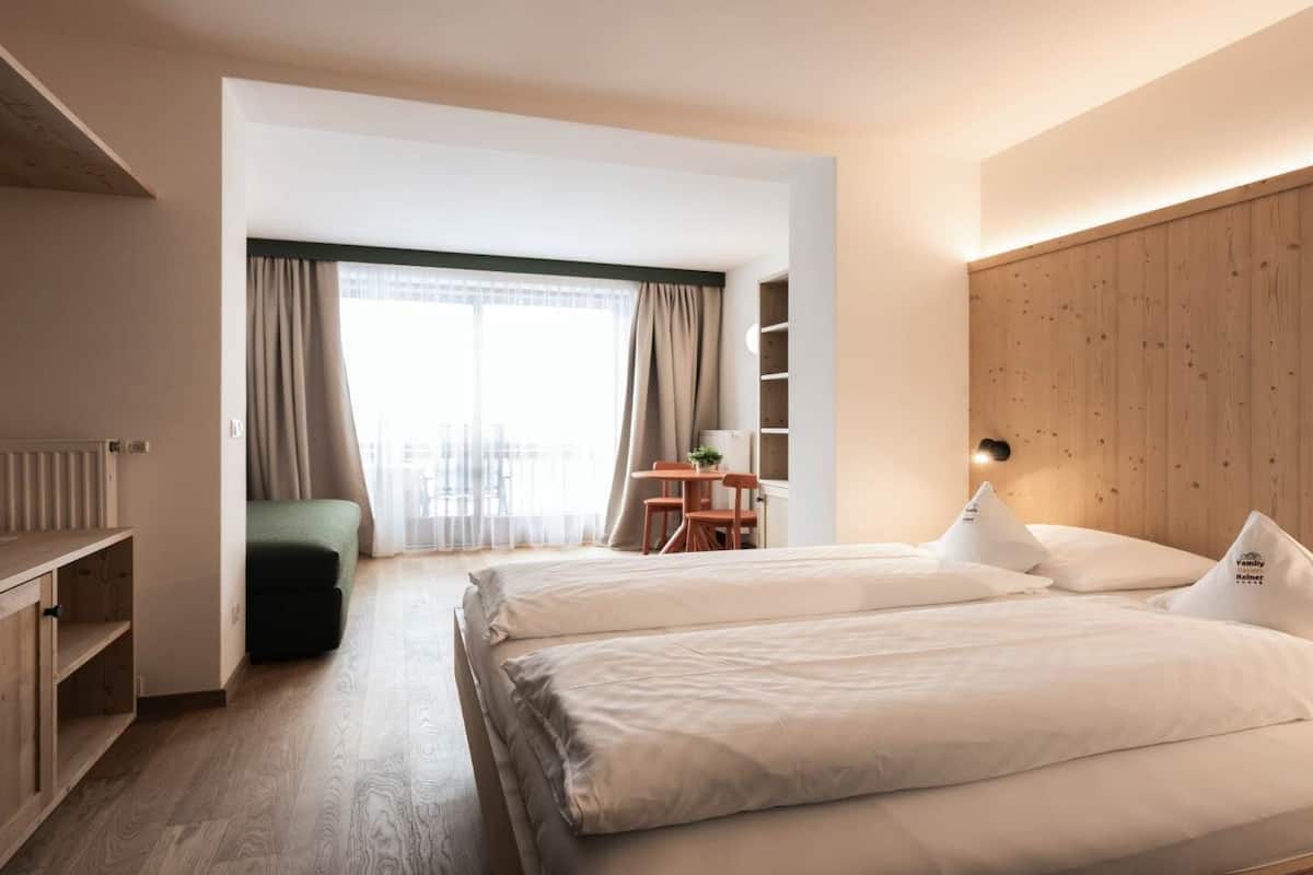 A modern hotel room with two beds, a wooden headboard, a desk, and a view of the city through large windows.