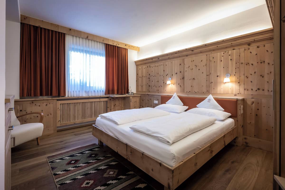 A wooden-paneled room with a bed, a chair, and a window with curtains.