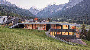 A modern house with a sloped roof, large windows, and a view of mountains. - Family Resort Rainer (Sesto)