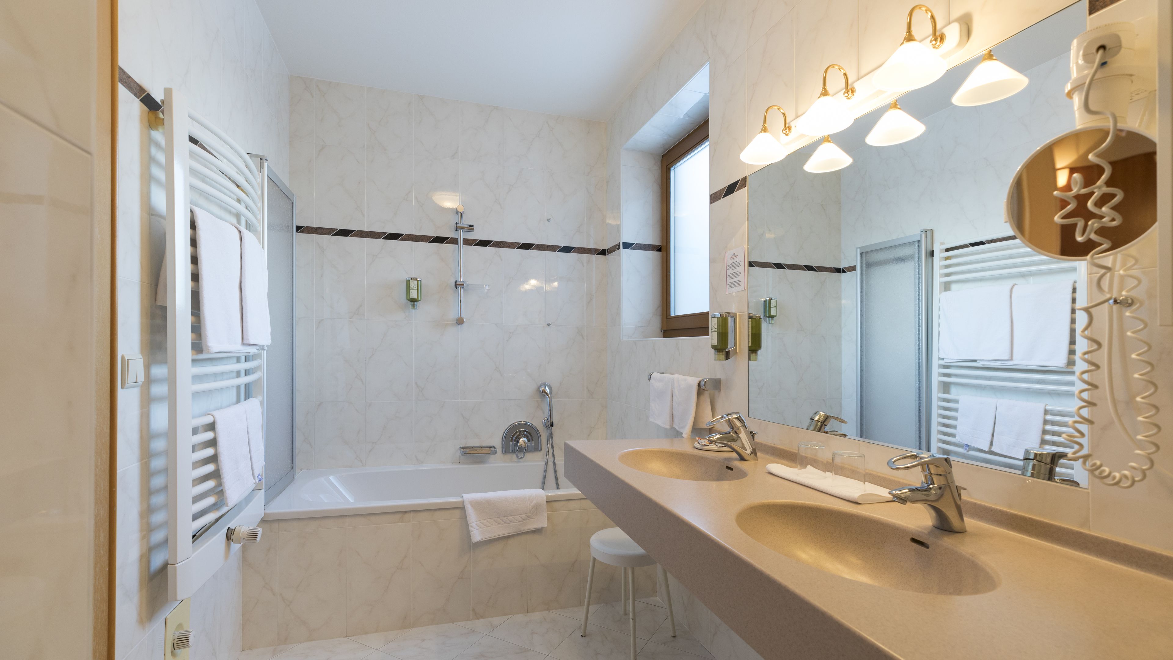 A modern bathroom with a bathtub, a large vanity with a sink, and a mirror. There are towels hanging on the wall and a showerhead above the bathtub.