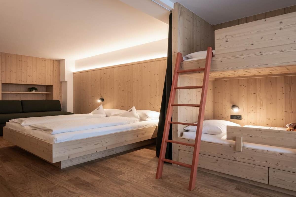 A room with two bunk beds, a ladder, a sofa, and a small shelf with a plant.