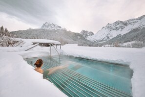 A person in a glass-bottomed pool surrounded by snow-covered mountains and trees. - Family Resort Rainer (Sesto)