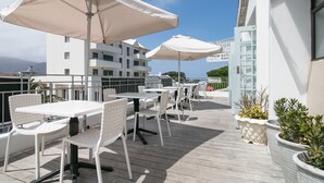 A deck with white tables and chairs, large umbrellas, and potted plants. - Zzzone Boutique Hostel (Hermanus)