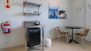 A compact kitchenette with a coffee maker, a fire extinguisher, and a small refrigerator. There are two wicker chairs and a round table. - Zzzone Boutique Hostel (Hermanus)