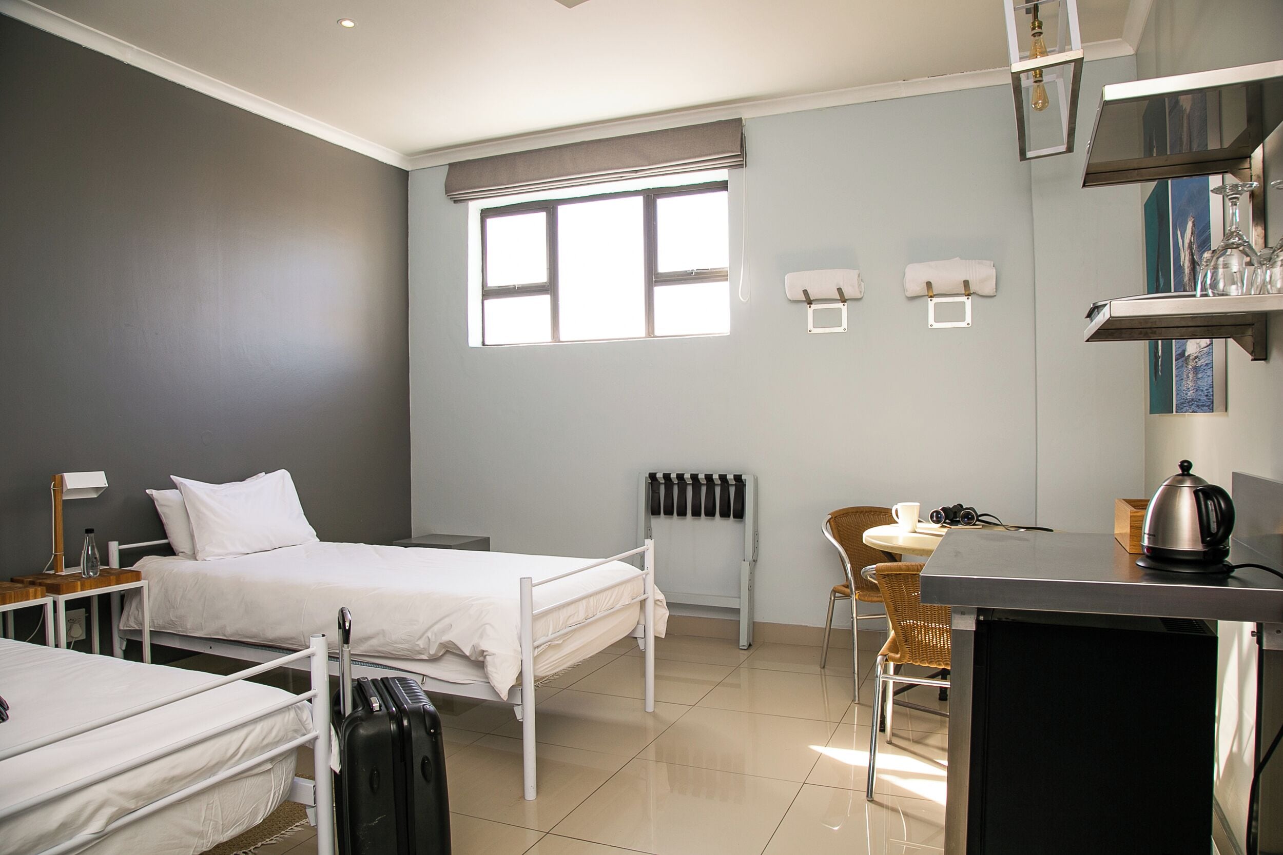 A hotel room with two beds, a desk, a chair, a radiator, and a window.