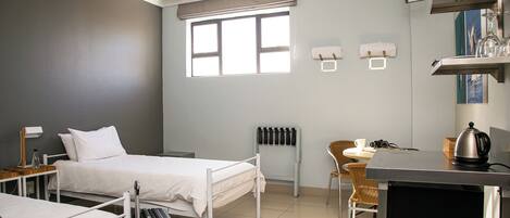 A hotel room with two beds, a desk, a chair, a radiator, and a window.