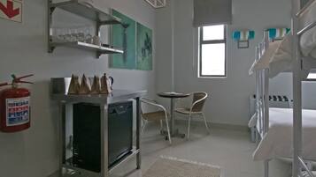 A hotel room with bunk beds, a small kitchenette, a table with chairs, a window, and artwork on the walls.