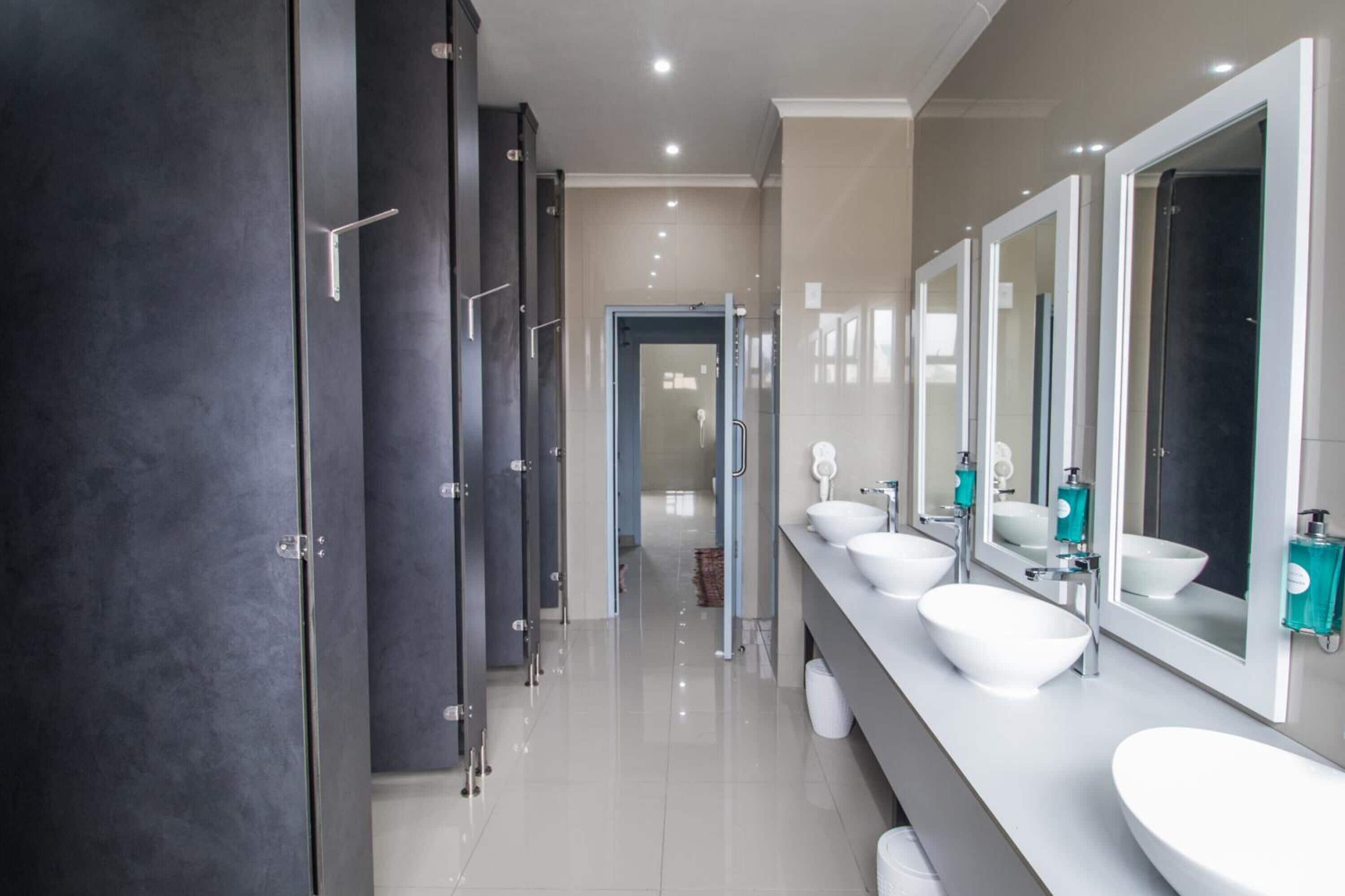 Un baño moderno con varios lavamanos, armarios oscuros y un espejo grande.