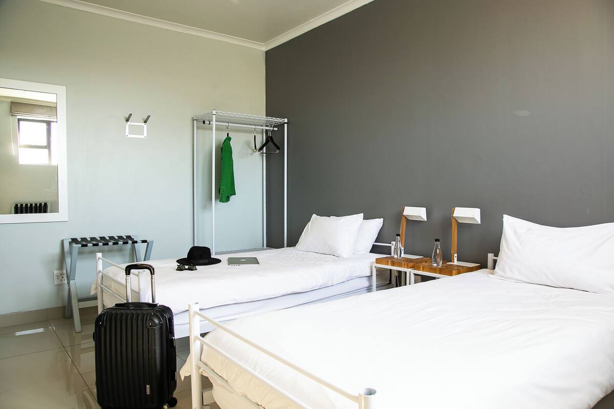 A hotel room with two beds, a suitcase, a coat rack, and a small table with a lamp.