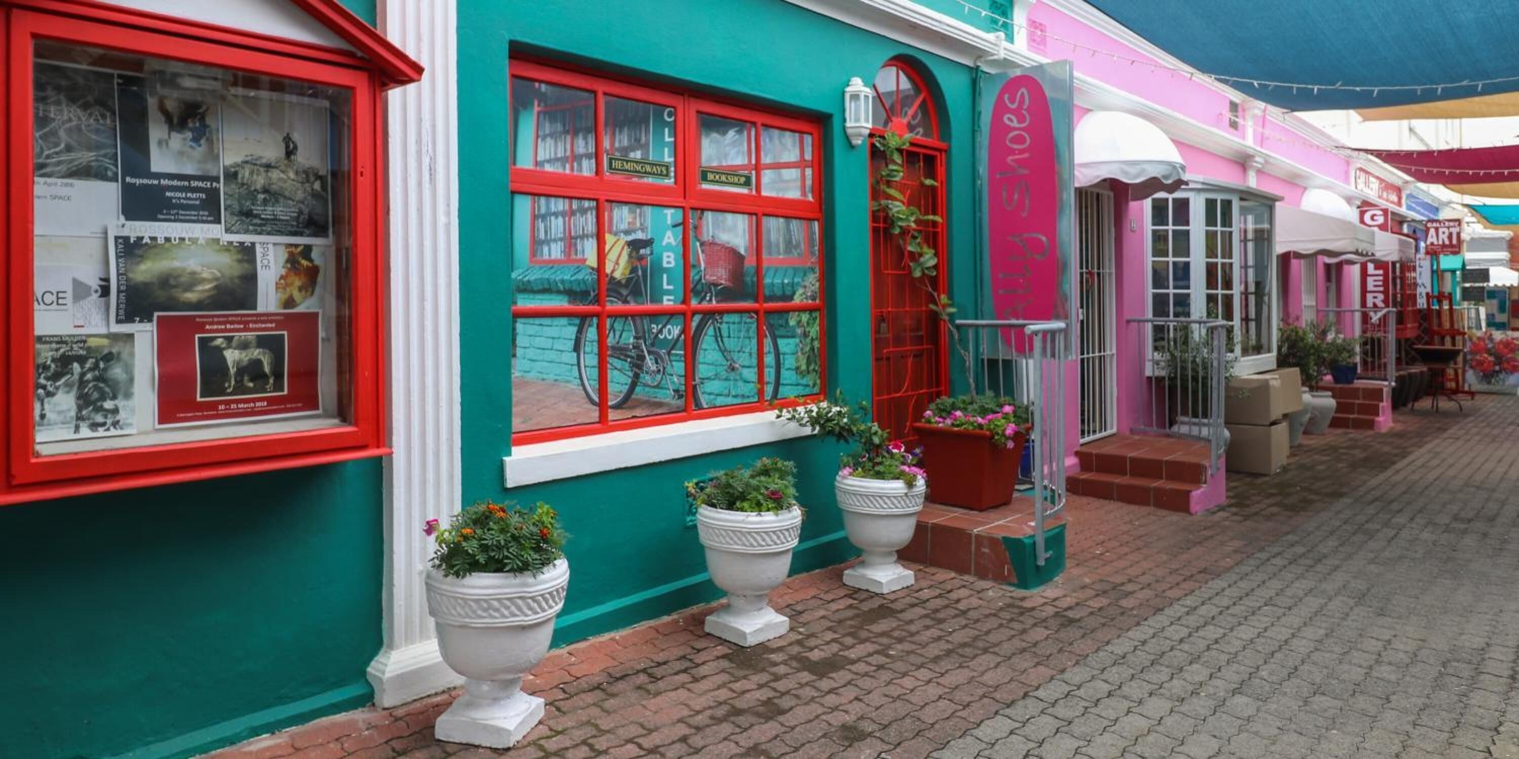 En farverig butiksfacade med et rødt vinduesramme, plantekasser og et skilt med 'The Shoe Gallery'.