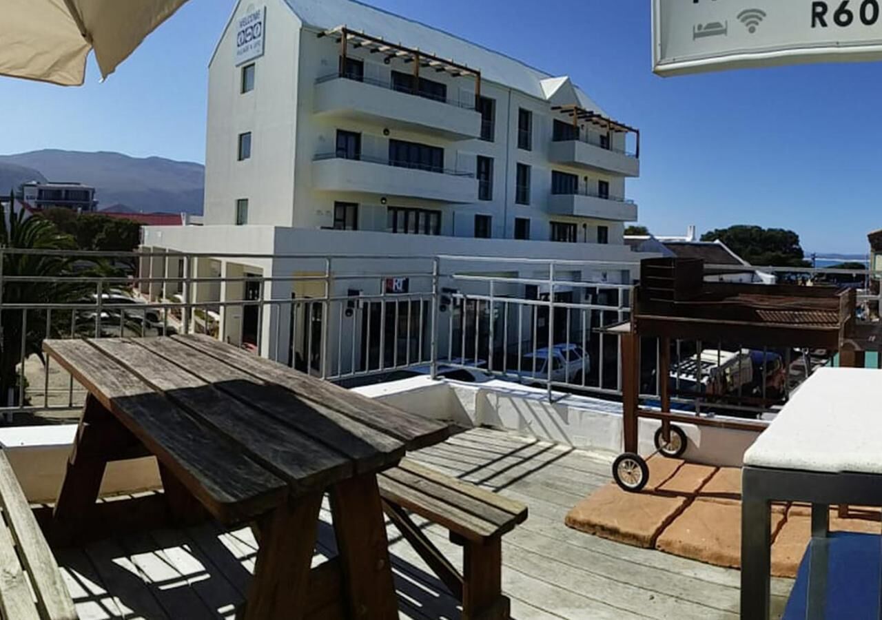 A rooftop terrace with wooden tables and a view of a white building with balconies.