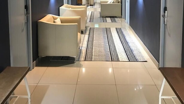 A modern hallway with a central seating area, recessed lighting, and a patterned rug. - Zzzone Boutique Hostel (Hermanus)
