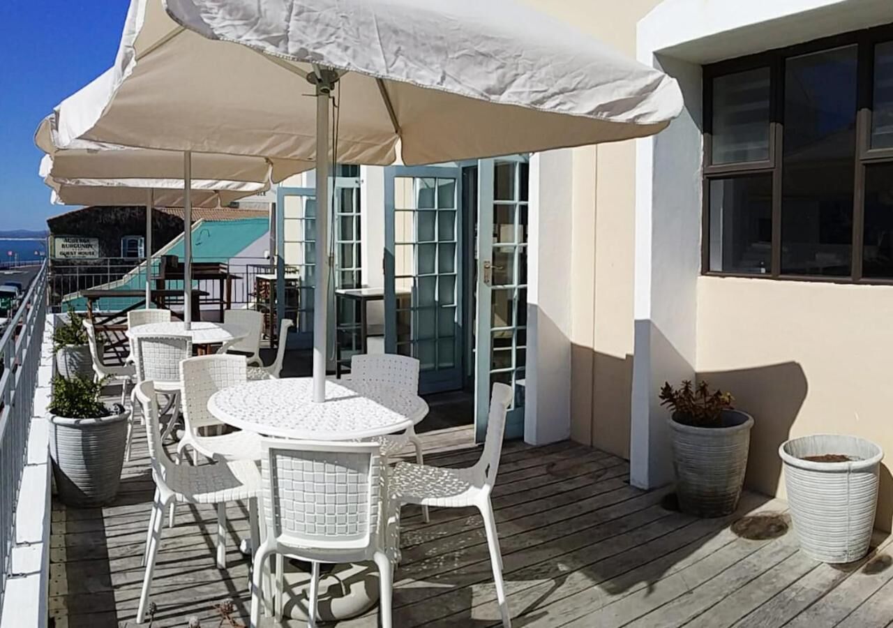 A deck with white wicker furniture, including round tables and chairs, under a large white umbrella.