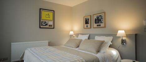 A neatly made bed with a checkered blanket, two bedside lamps, and framed pictures on the wall.