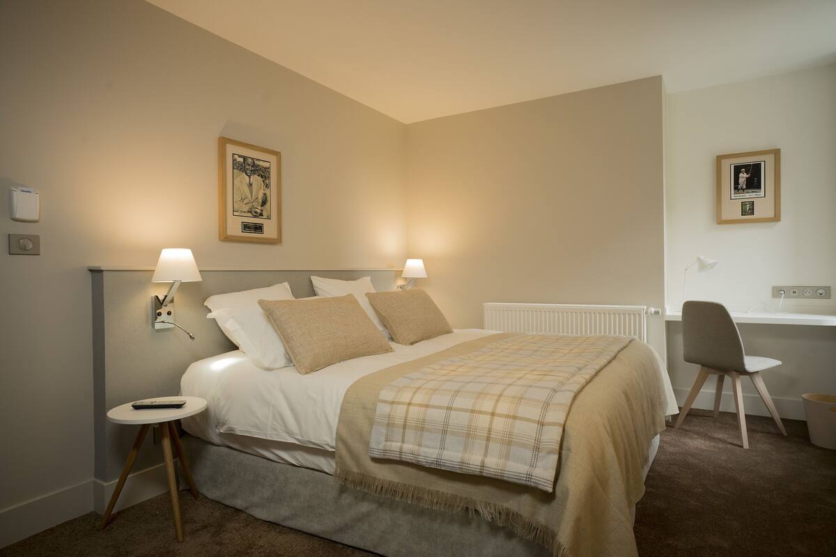 Een slaapkamer met een bed, nachtlampjes, een stoel, een klein tafeltje en een radiator.
