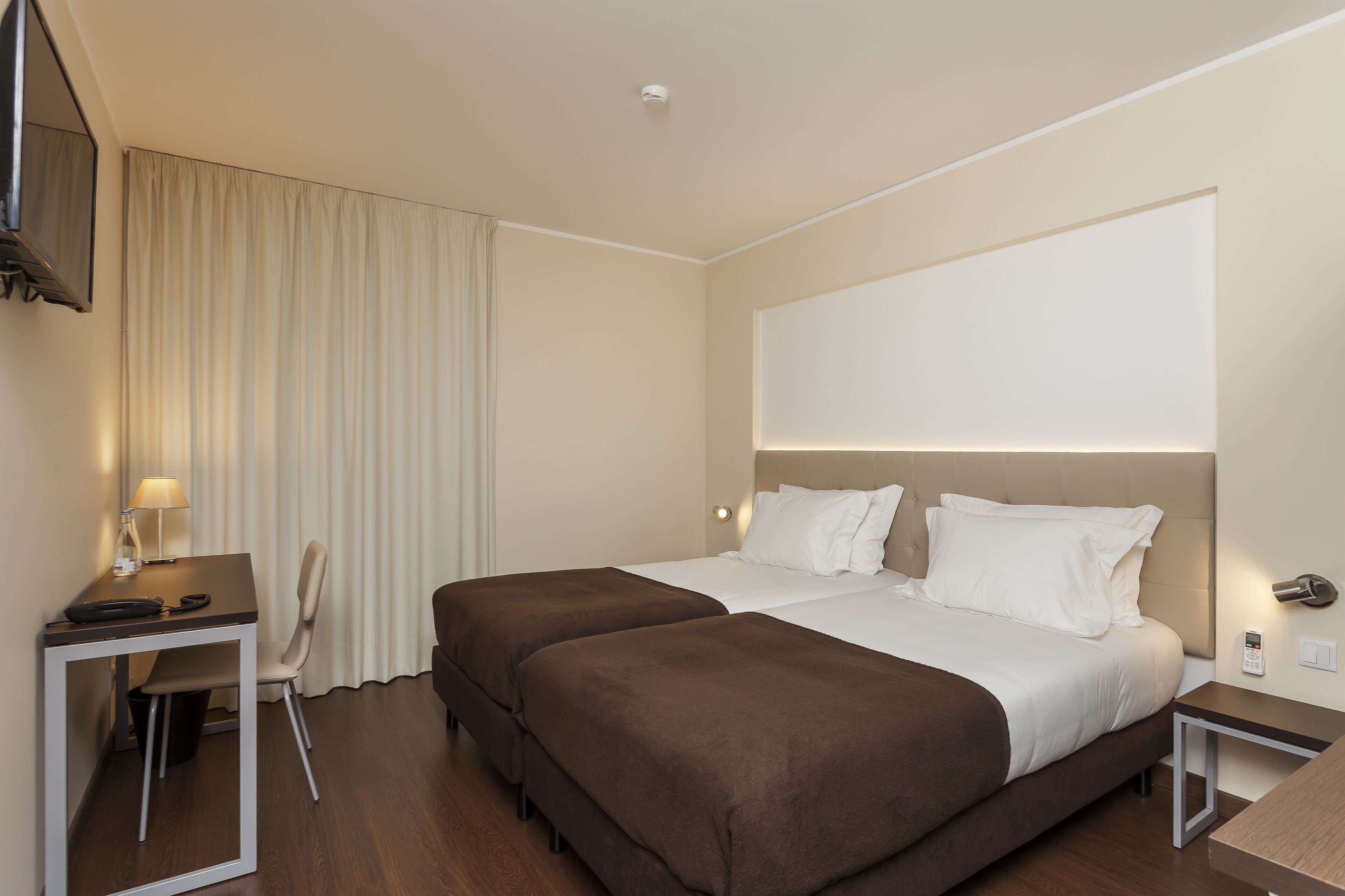 A hotel room with two beds, a desk, a chair, and a TV.