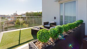 A balcony with a glass railing, a wicker sofa, a small table, and a potted plant. - In Gold Hotel & Spa (Agueda)