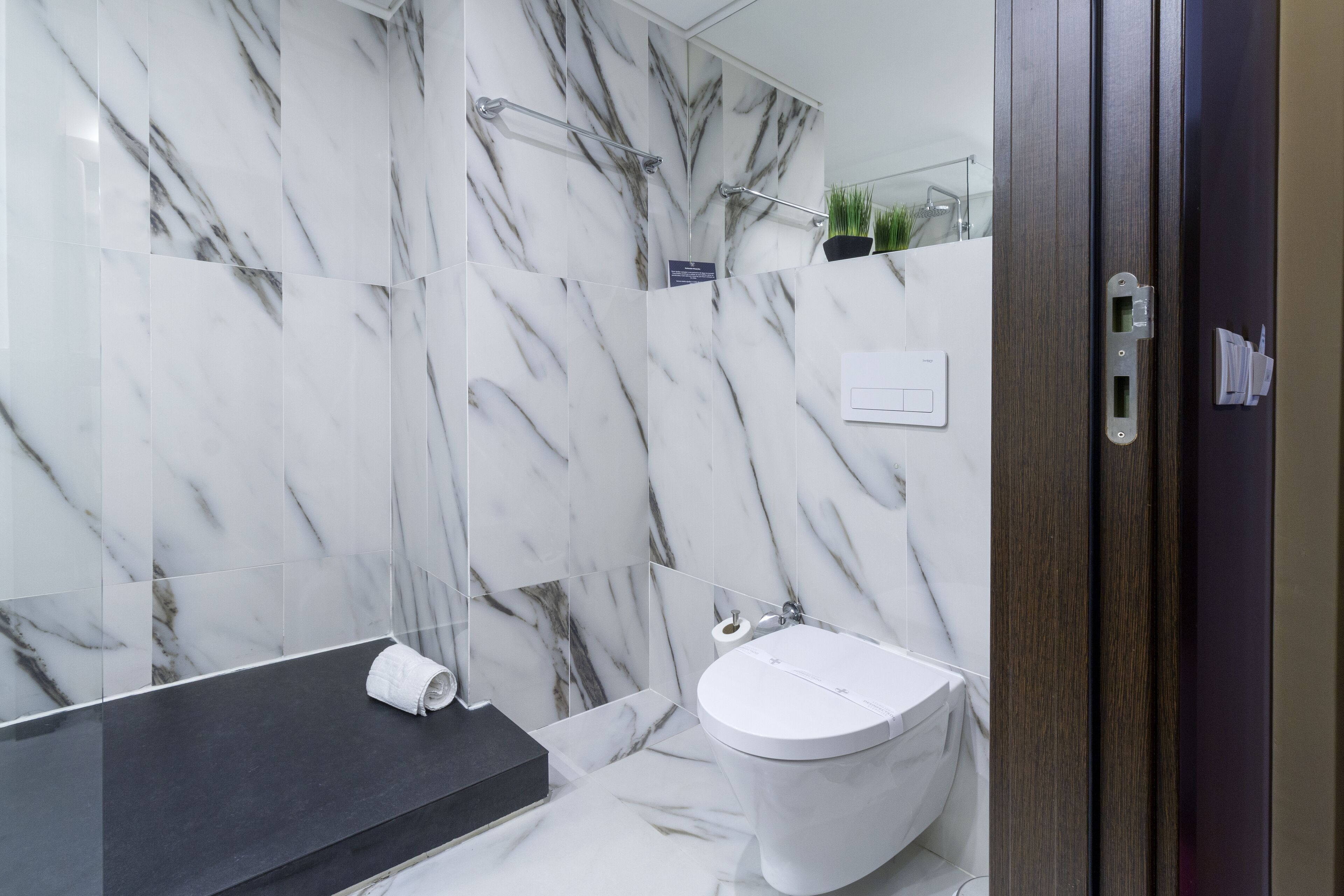 A bathroom with a marble wall, a black countertop, a white toilet, and a wooden door.