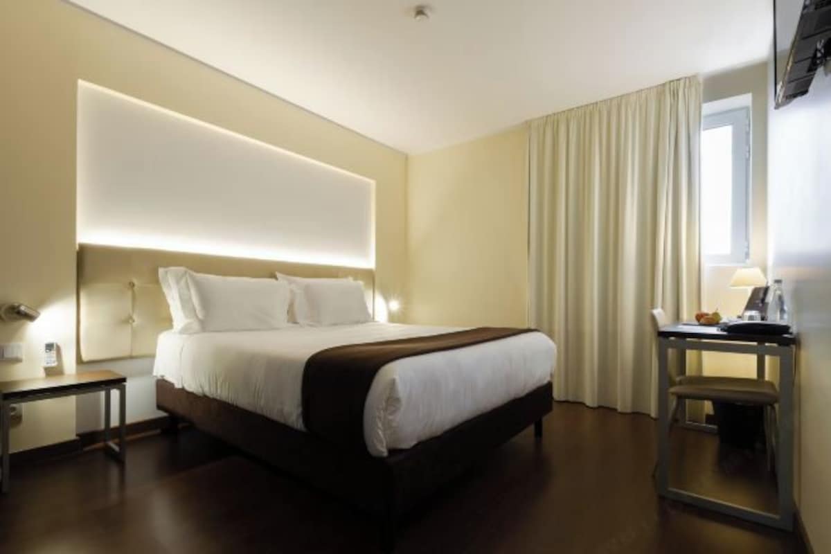 A hotel room with a large bed, a desk, and a television.