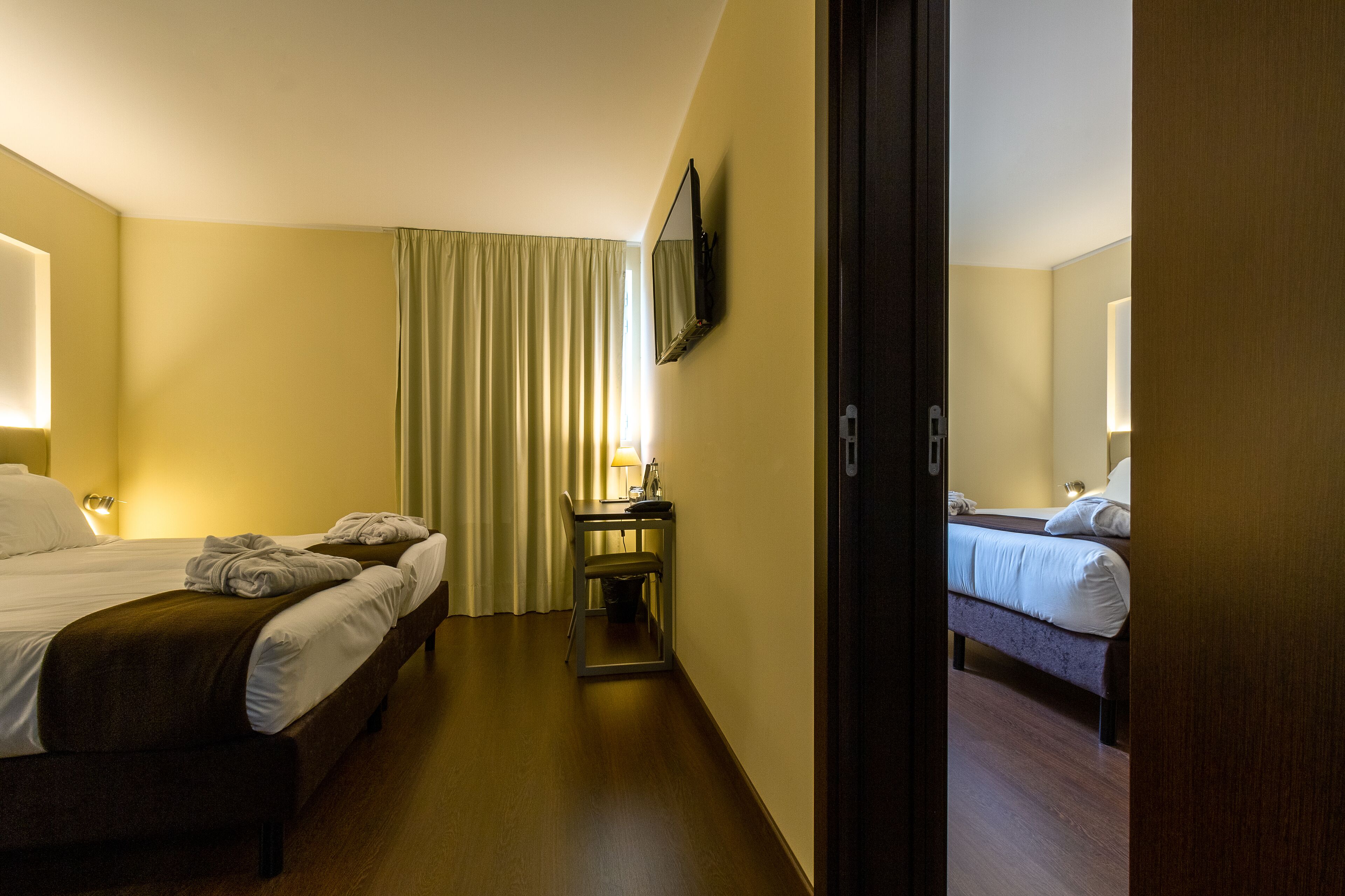 A hotel room with two beds, a desk with a lamp, and a television mounted on the wall.