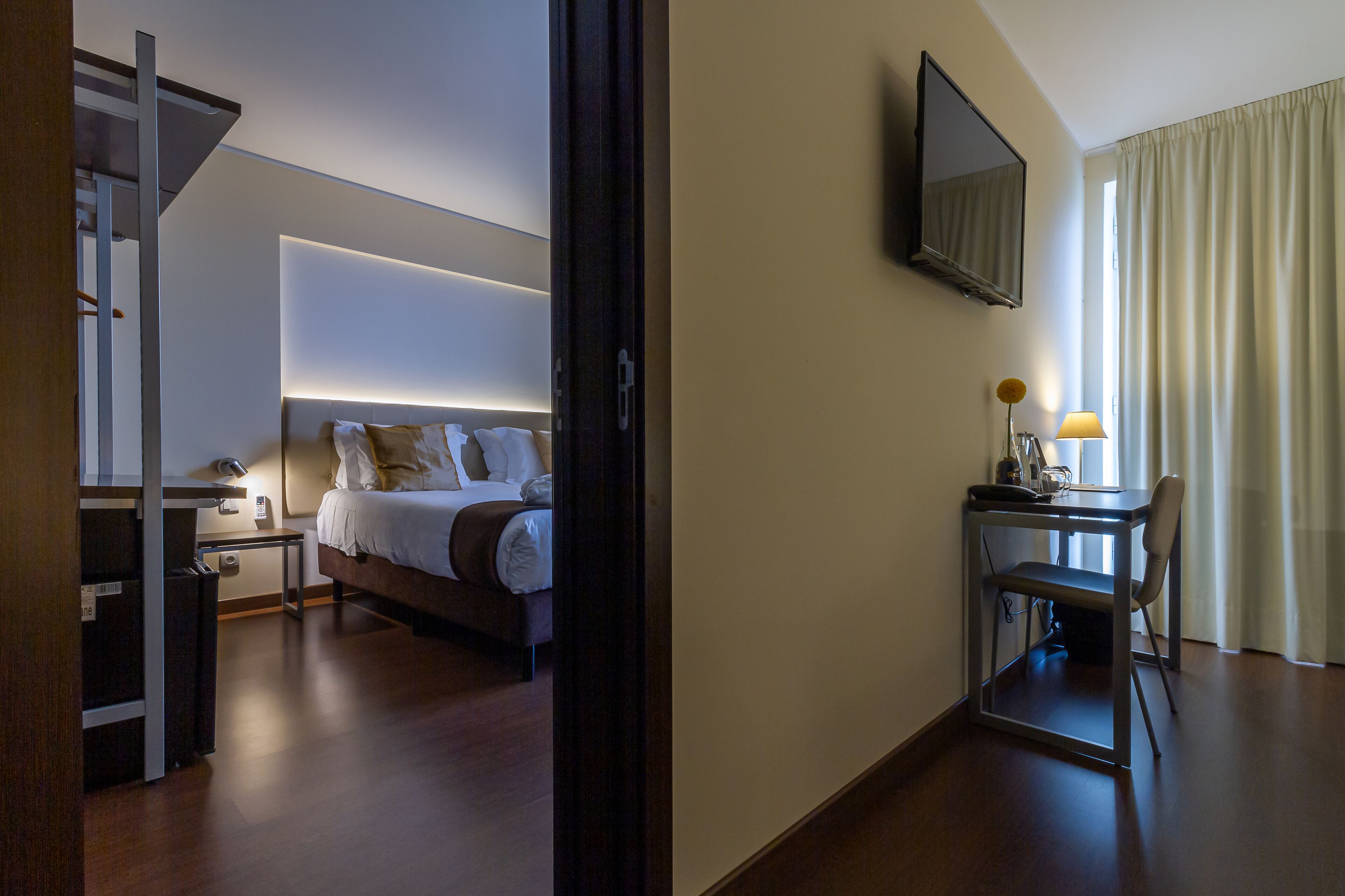 A modern hotel room with a bed, bedside table, and a desk with a chair.