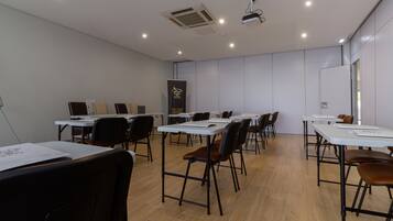Un salón de conferencias con varias mesas y sillas, equipado con proyectores de techo y unidades de aire acondicionado.