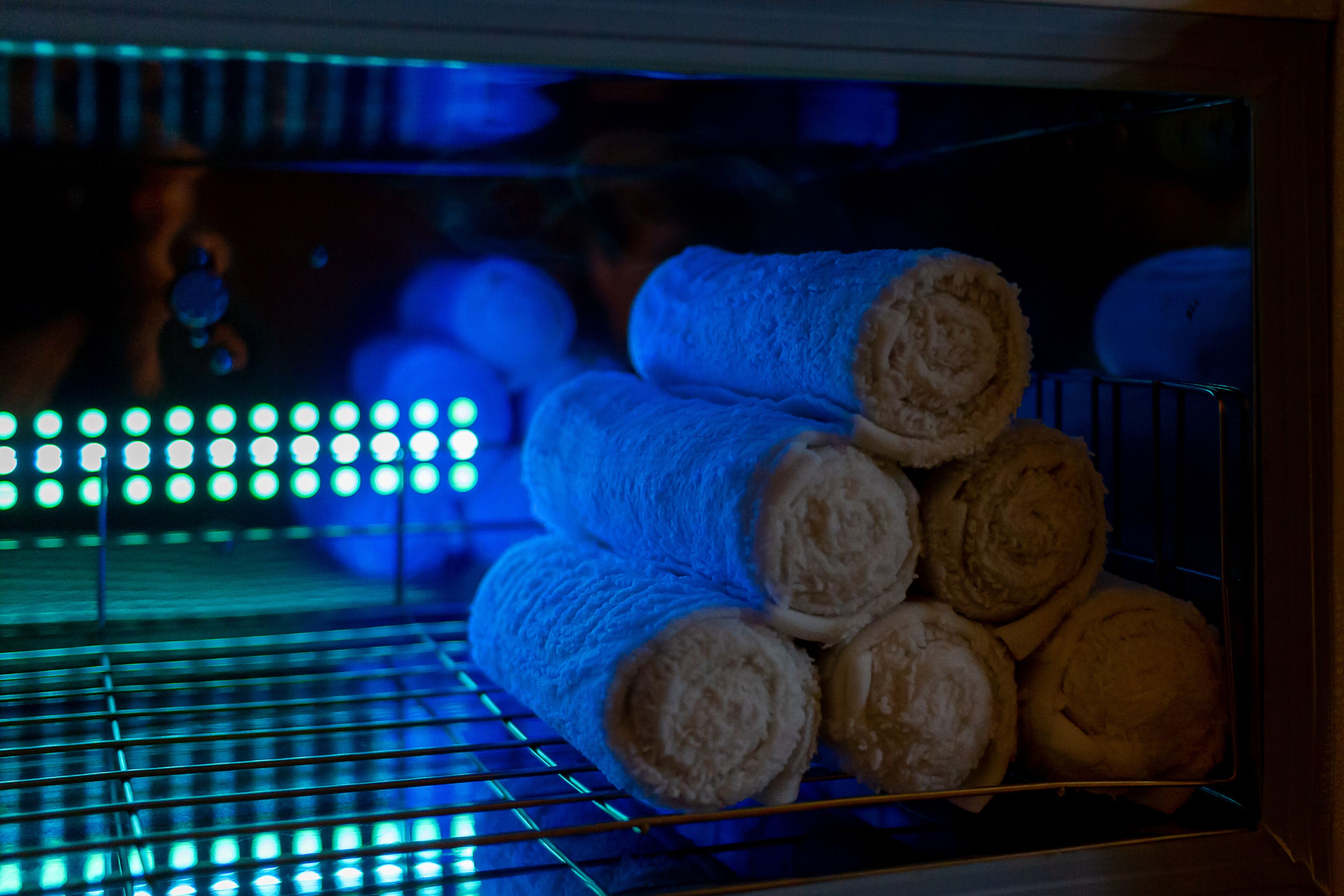 A stack of rolled towels in a metal rack inside a room with blue lighting.