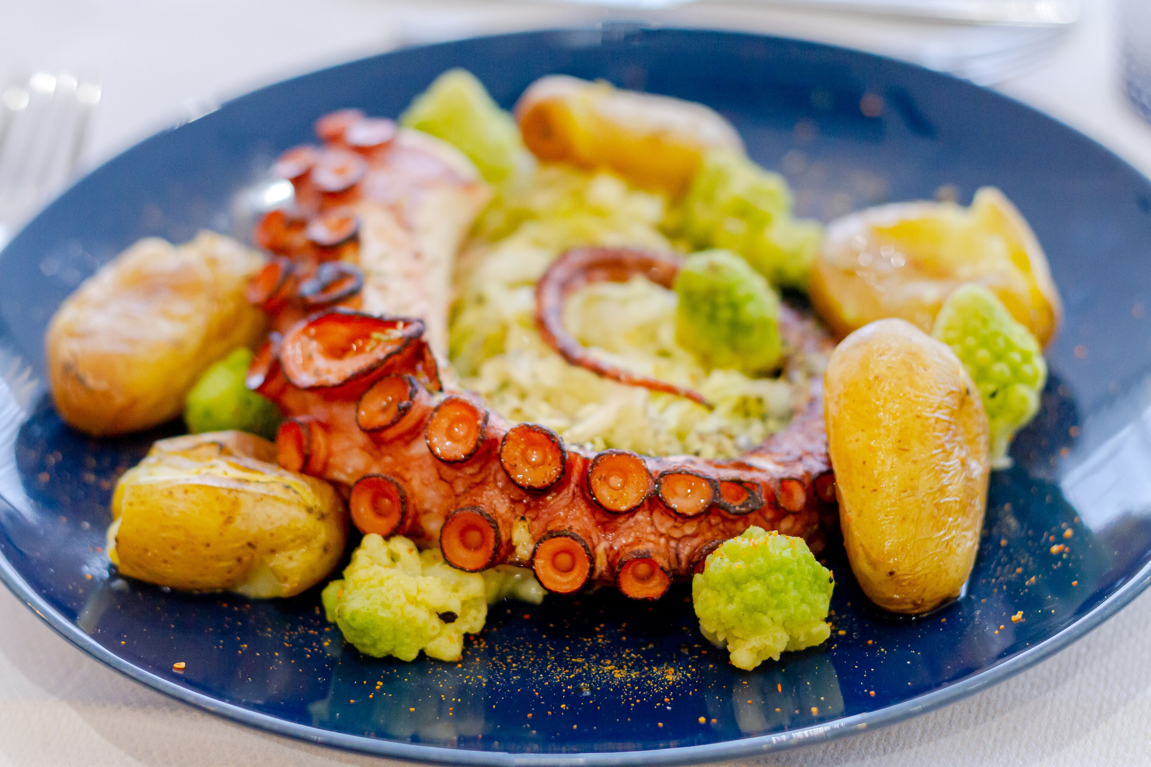 Un plato de pulpo con papas y verduras verdes.