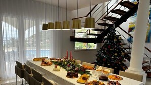 A dining area with a long table set for a meal, a Christmas tree, and a staircase.