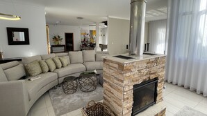 A modern living room with a stone fireplace, a curved sofa, and a dining area in the background.
