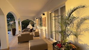 A sunlit corridor with a sofa, ottoman, and potted plants.