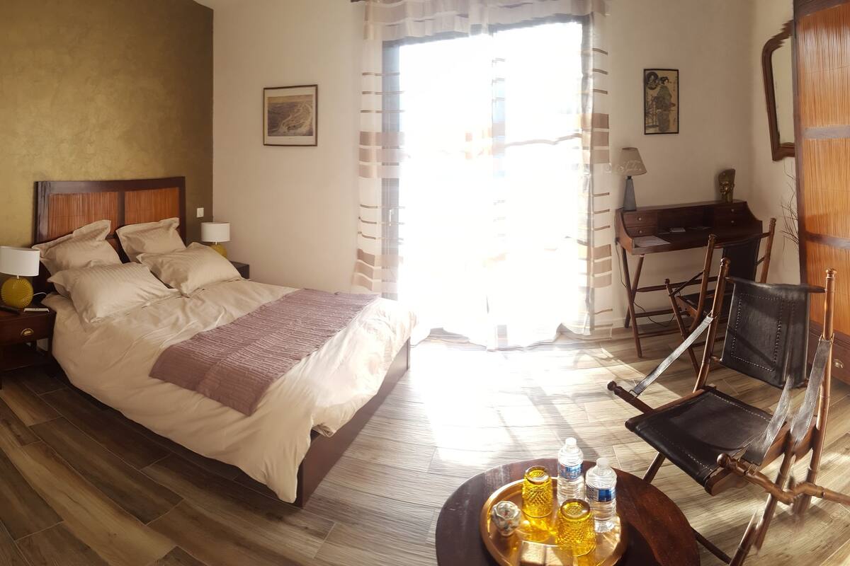 A hotel room with a bed, bedside tables, a desk, a chair, and a window with curtains.