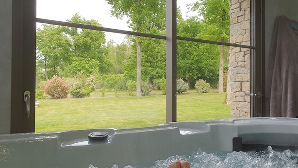 A bathroom with a bathtub, a towel hanging on the wall, and a view of a lush garden through large windows. - La Vertabelle (Vertou)