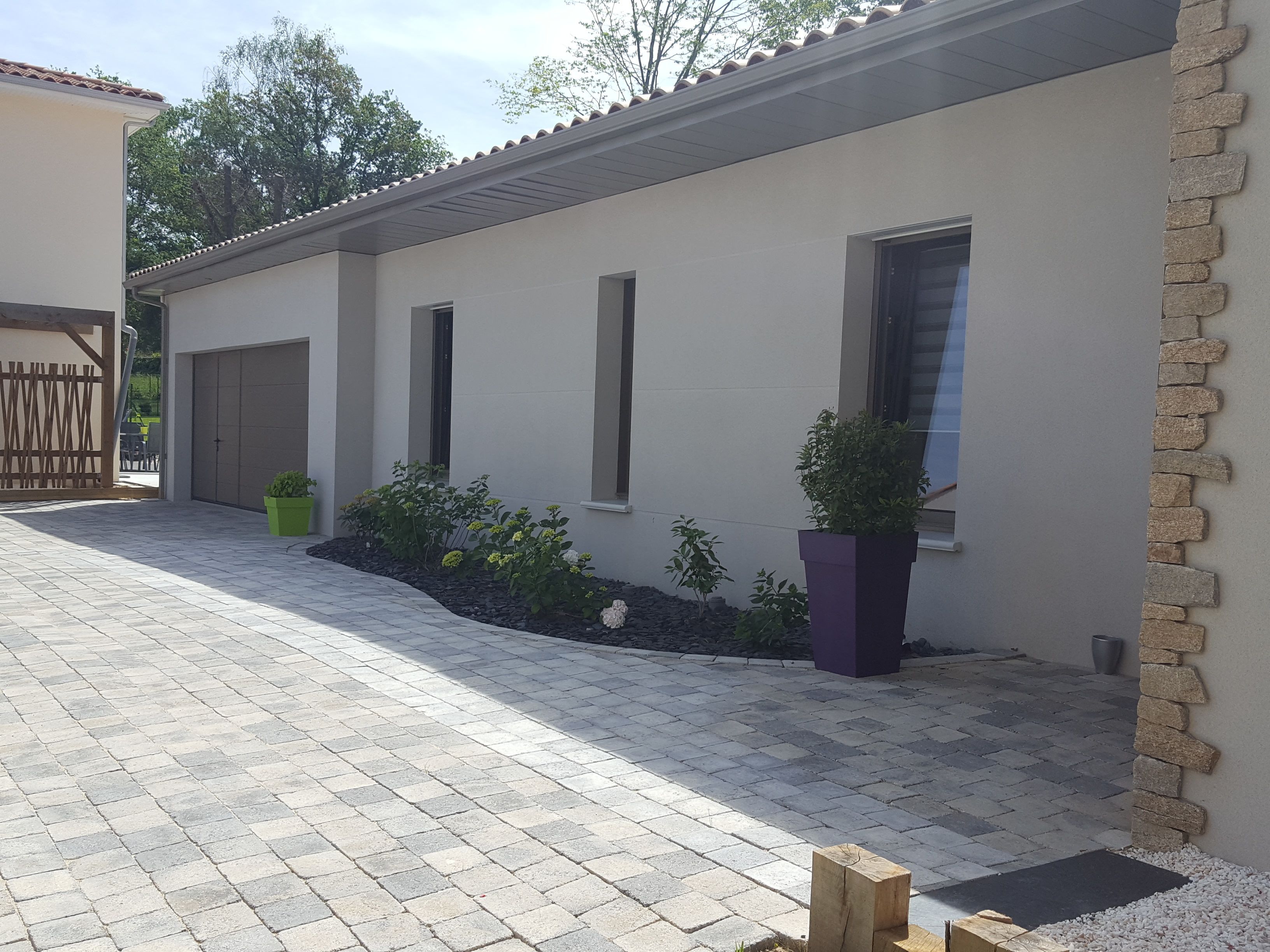 Ein modernes Haus mit befestigter Auffahrt, Garage und kleinem Garten mit Kübelpflanzen.