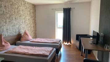 Ein Hotelzimmer mit zwei Betten, einem Schreibtisch mit Computer und einem Fenster mit Vorhängen.