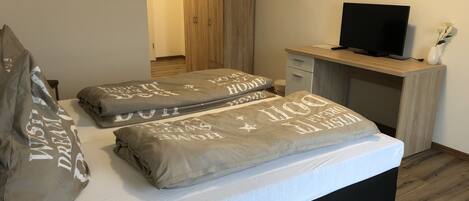 Un dormitorio con cama, almohadas, televisor y escritorio.