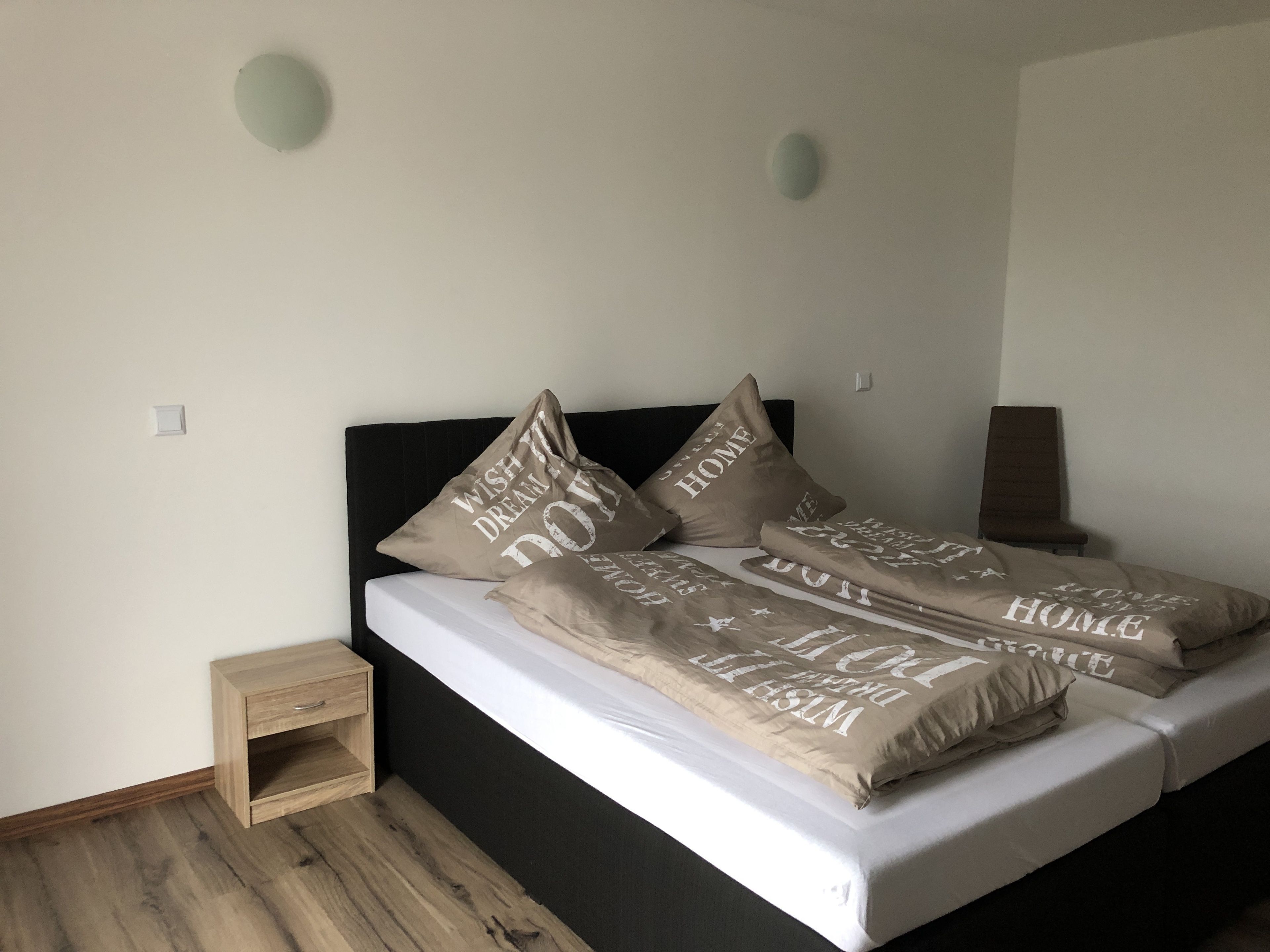 A bed with multiple pillows, a bedside table, and a small wooden nightstand.